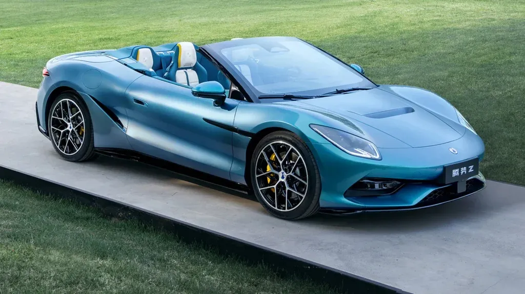 Blue convertible sports car parked on a concrete platform with a grassy lawn in the background, open-top with white and blue seats visible.] , ...