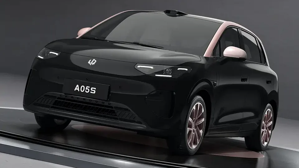 Angled view of a black compact hatchback with pink roof pillars, showing front grille and headlights, license plate reads A05S, on a showroom stand.