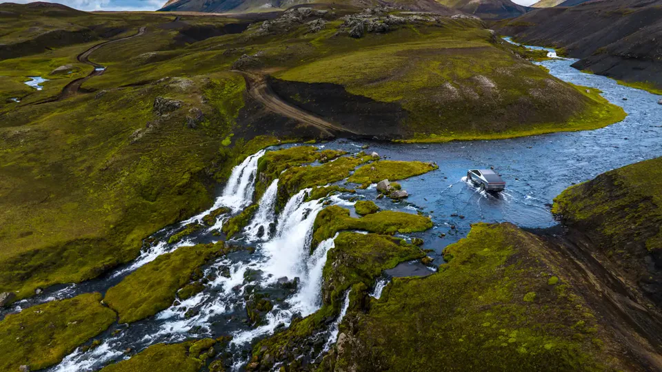 Elettronauti - Tesla Cybertruck argento che attraversa un fiume in una veduta aerea